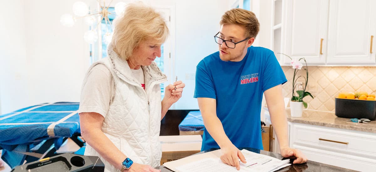 Port City Movers employee reviewing moving paperwork with a customer in kitchen.