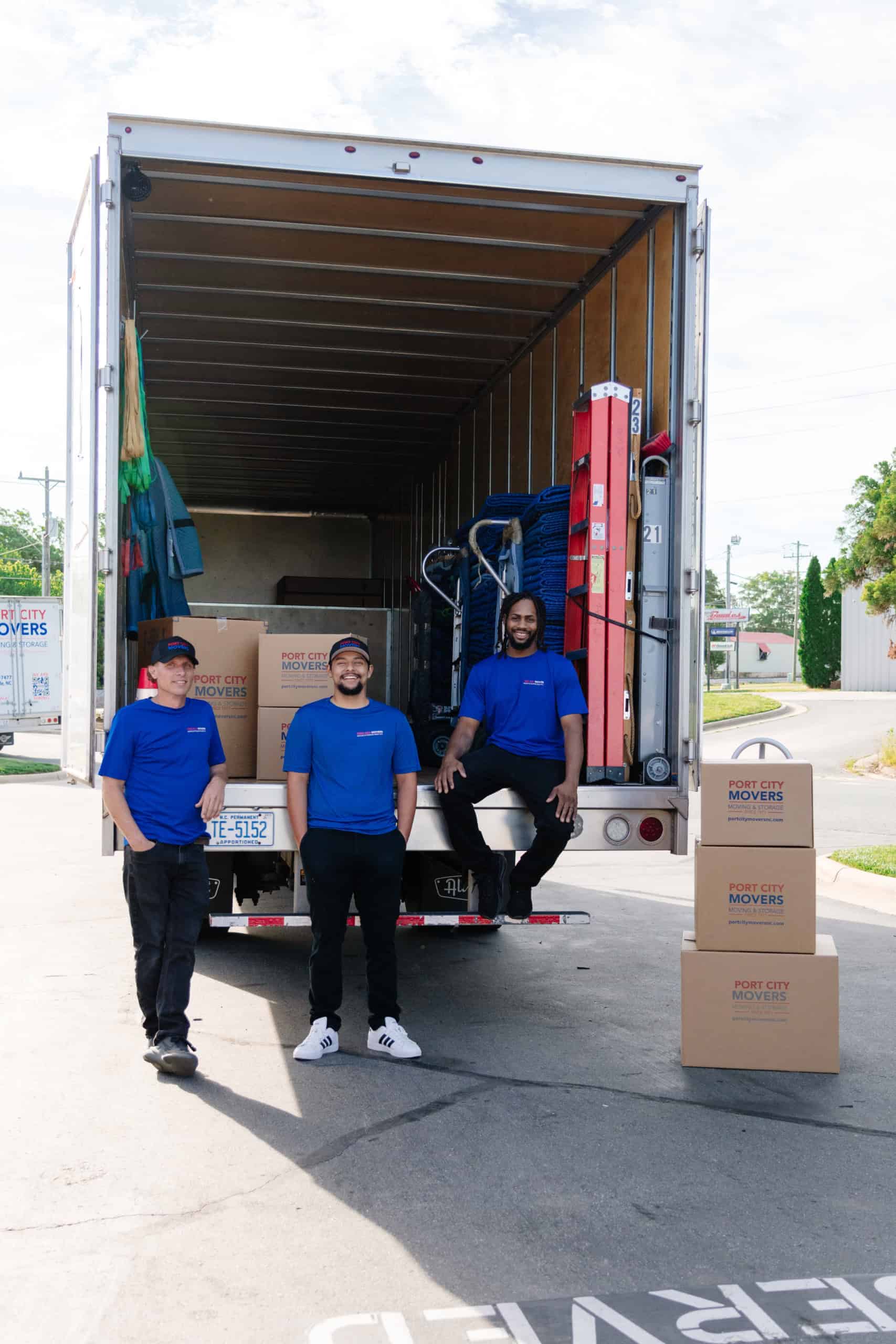 Three Port City Movers employees standing near the back of a moving truck with boxes stacked around them.